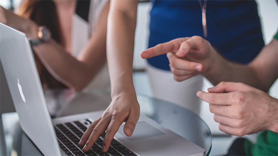 three people pointing at a silver laptop screen; image used for blog post about not-for-profit computer programs