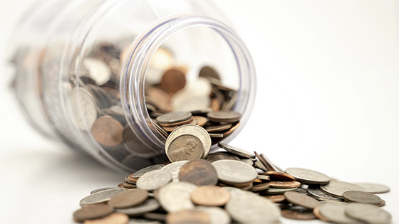 coins--pennies, quarters, dimes and nickels--pouring out of a glass jar into a pile; image used for blog post about answers for Economic Impact Payments during the COVID-19 pandemic