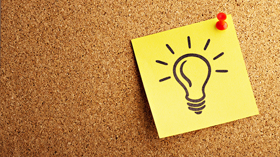 yellow sticky note with a drawn light bulb thumbtacked to a cork board; image used for blog post about how to promote a not-for-profit in 201