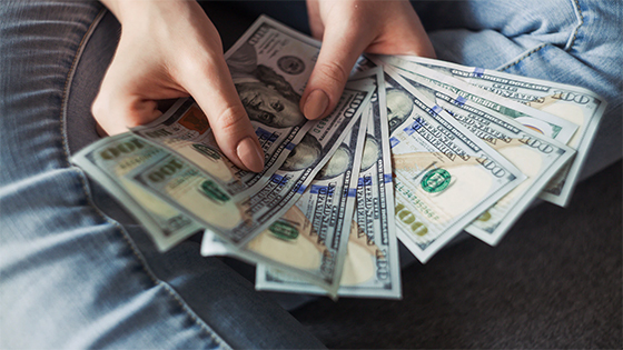 woman holding hundred dollar bills fanned out; image used for blog post about commerciality doctrine for not-for-profits
