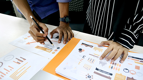 two women writing on papers with data and pie charts on a table; image used for blog post about not-for-profits reaching out to high-net-worth individuals for funding