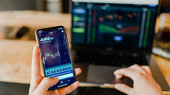 person typing on a computer with stats and graphs while also holding a phone with stats; image used for blog post about deductible expenses for owning investment portfolio