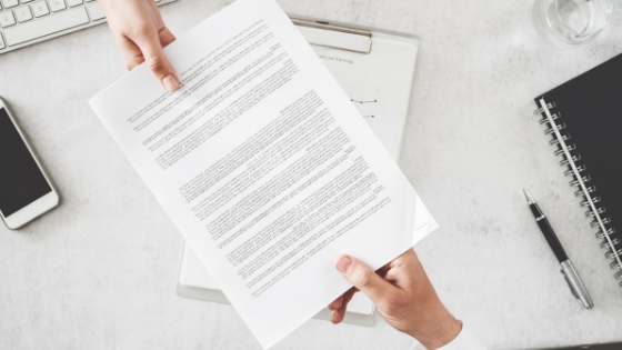 One person handing a document to another person over a table; image used for blog post about substantiation for charity donations