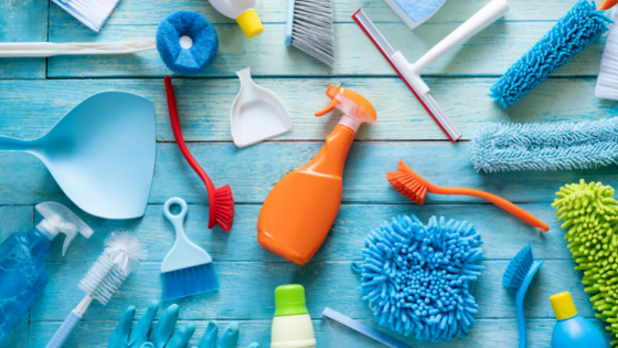 A wooden table with various cleaning tools and supplies, such as brushes, spray bottles, scoops, and more; image used for blog post about not-for-profit programming spring cleaning