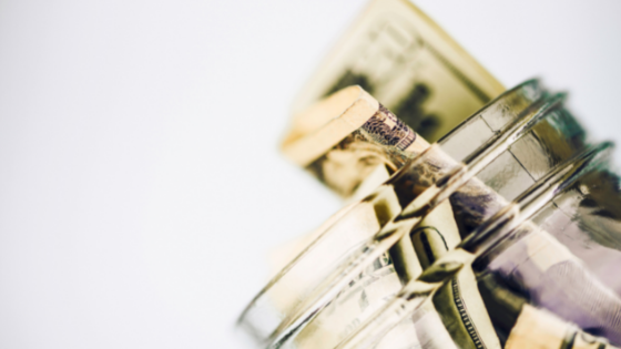 close up view of a glass jar with cash popping through the top; image used for blog post about matching gift donations