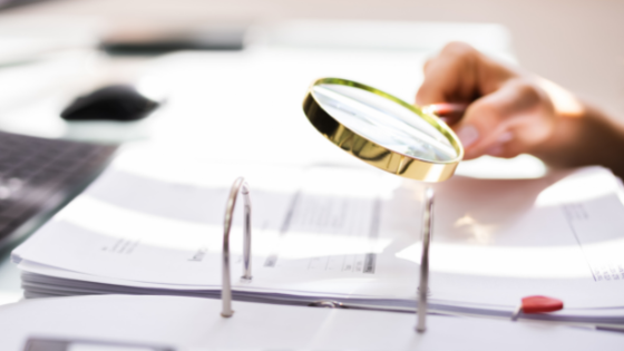 A photo of someone looking at financial statements with a magnifying glass; image used for blog post about limiting fraud in not-for-profits