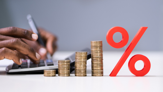 A photo of someone typing on a calculator next to coins and a large percentage sign figure; image used for blog post about high-income extra taxes