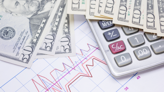 A photo of a calculator and dollar bills sitting on top of a document with red spike lines; image used for blog post about inflation impacting 2022 and 2023 tax bills