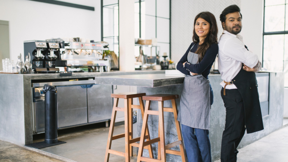 A photo of two people posing back to back in front of a coffee bar; for blog post about hiring your children for tax advantages