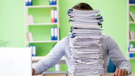 A photo of someone looking at a computer screen with a stack of papers covering their face; for blog post about what to do after you file your tax return