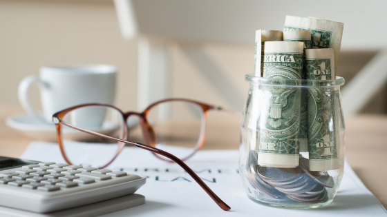 An image of a calculator, reading glasses and a jar of dollar bills sitting on a retirement plan document; for blog post about tax implications of retiring