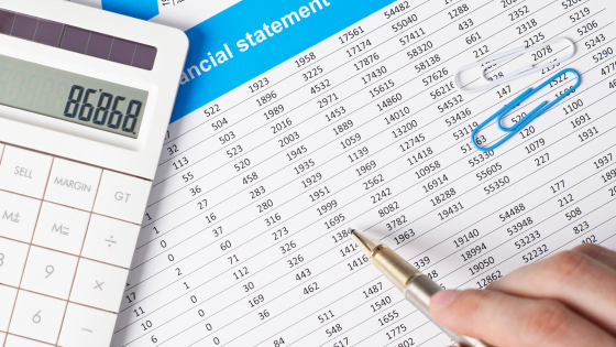 A photo of someone pointing a pen point to a financial document with numbers in rows