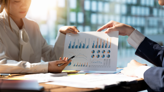 060923 – How You Can Reduce the Impact of the NIIT – 560×315 A photo of two people holding a document with data; for blog post about reducing impact of NIIT