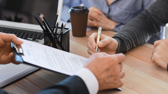 062623 – Consider an IRA if You’re Married and Not Earning Compensation – 560×315 A married couple signing an IRA financial document with an advisor