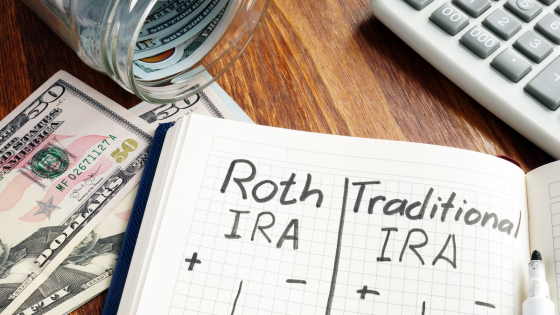 Photo of a notebook with written words, "Roth IRA | Traditional IRA" with dollar bills and a calculator; for blog post about catch-up contributions
